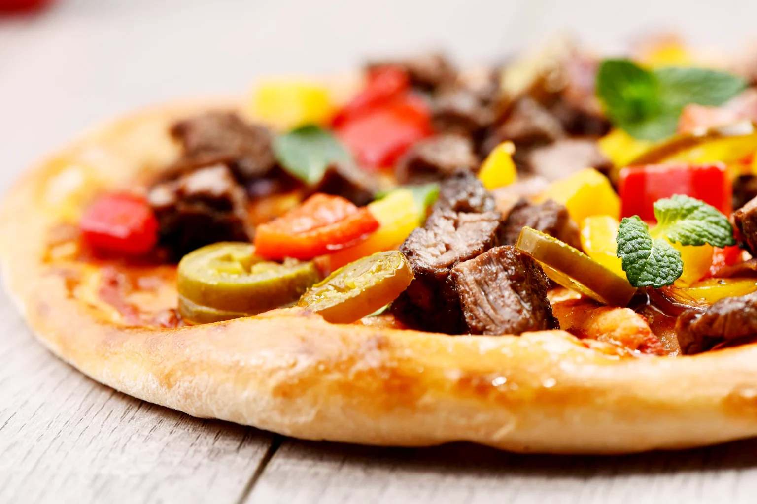 Nahaufnahme einer Pizza mit Tomaten, Oliven, Fleisch und Kräutern.