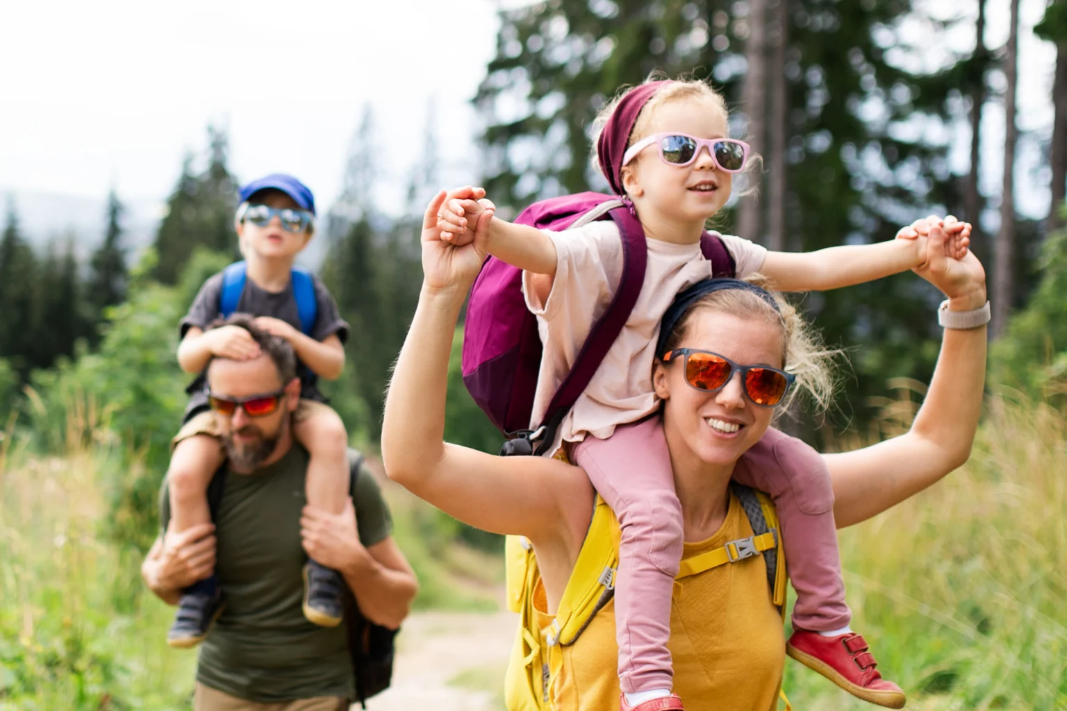 Junge Familie mit zwei Kindern die auf den Schultern ihrer Eltern sitzen.