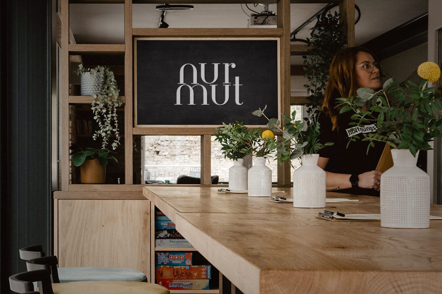 Innenansicht Café „nur mut“ mit Holztisch, Stühlen und Pflanzen