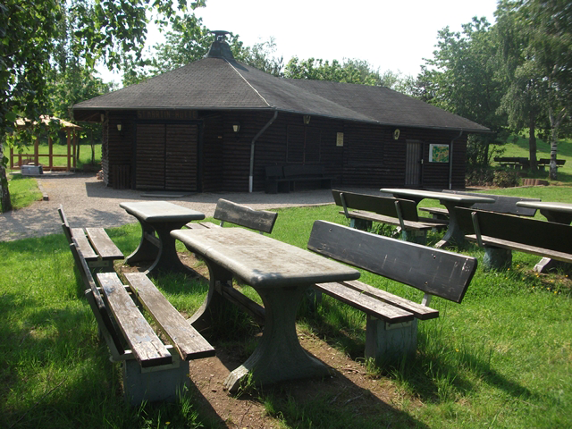 Bänke und Tische auf einer Wiese im Hintergrund eine geschlossene Holzhütte.